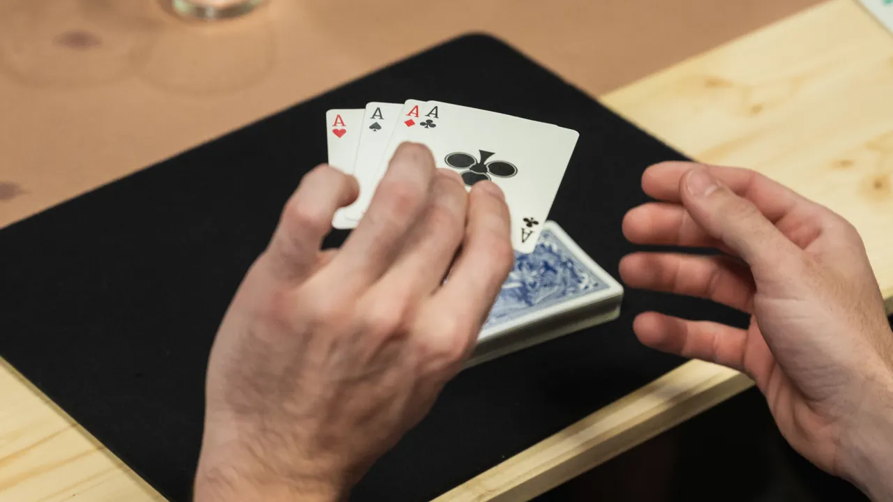 Hände halten vier Asse über einem Kartenspiel auf einem Holztisch